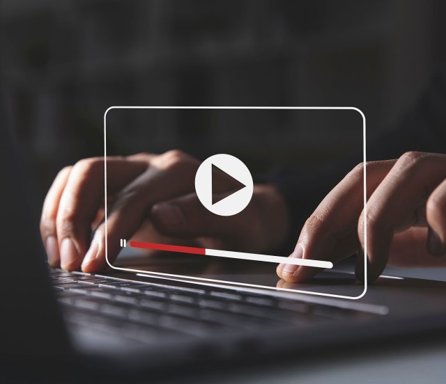 Close-up of hands typing on a laptop with an illustration of a video player icon
