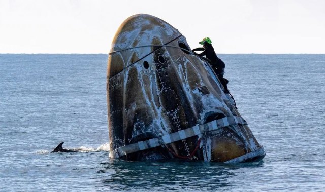 A support team member working on a capsule carrying astronauts that has landed in the ocean.