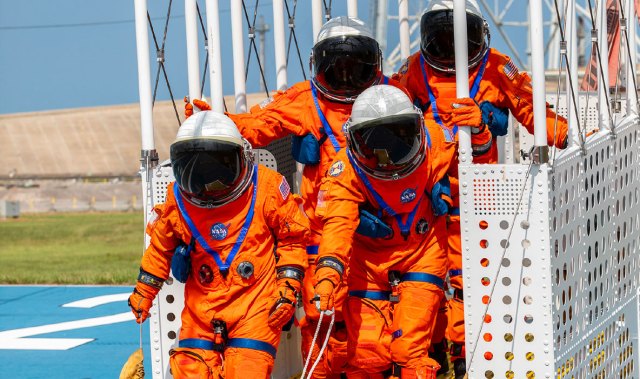 Astronauts in orange spacesuits practice getting out of an emergency escape basket.