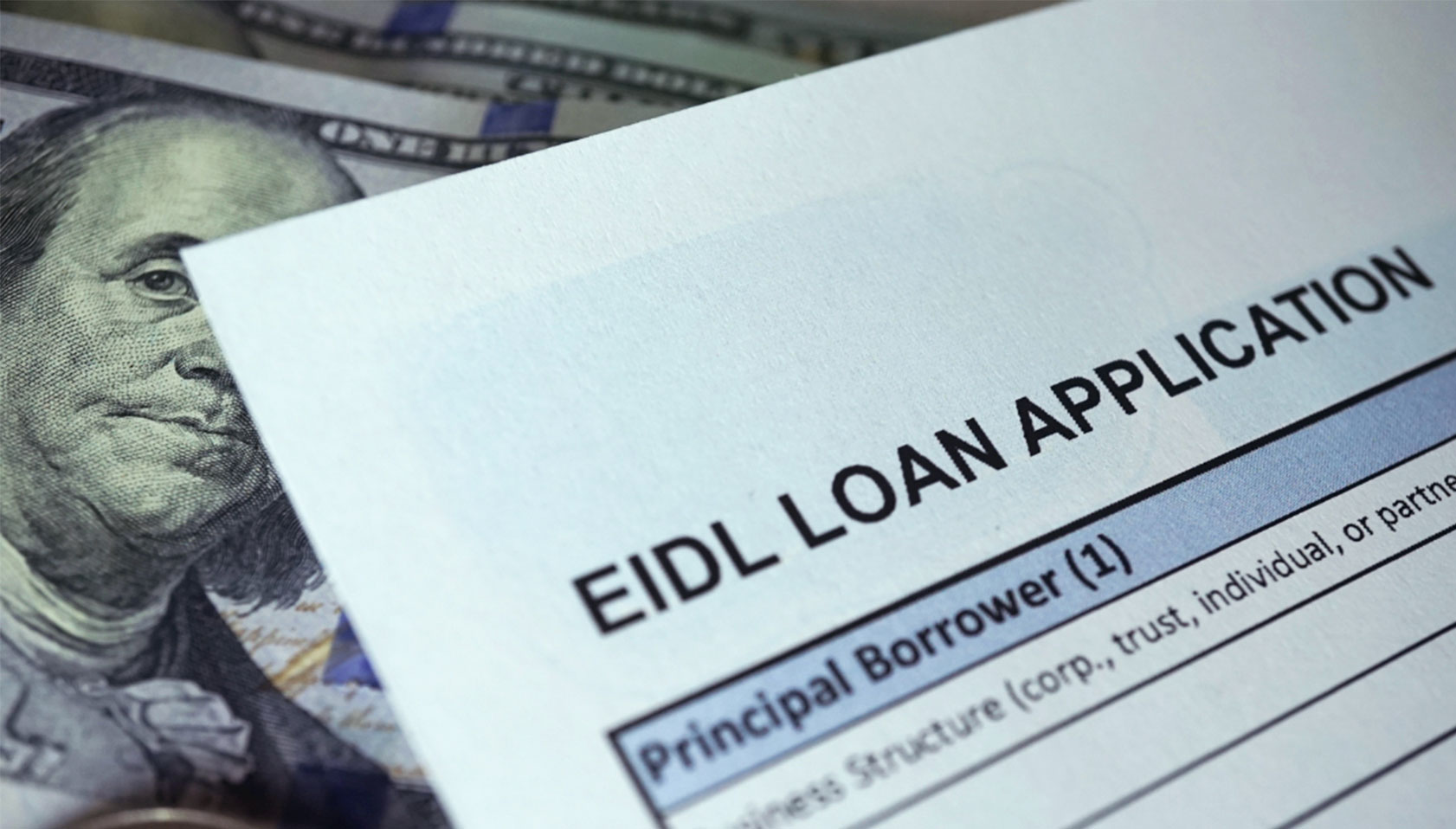An Economic Injury Disaster Loan (EIDL) application form on top of cash.