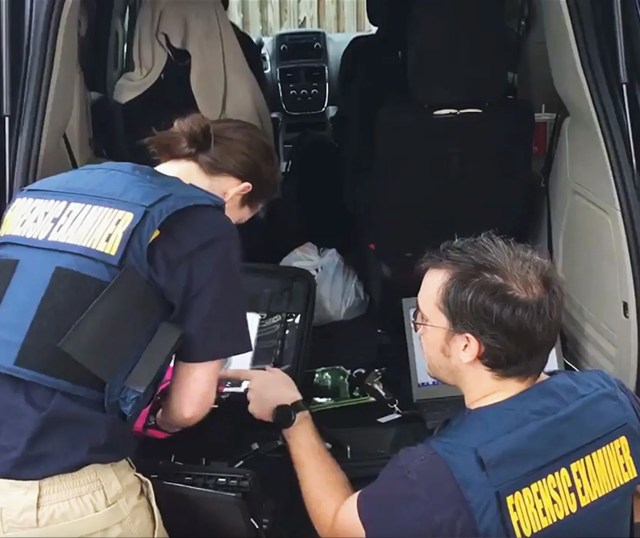 Forensic examiners looking at a computer in the trunk of a car