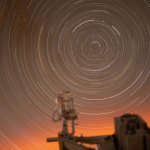 Star trails creating a circular pattern in an orange sky, viewed from a window inside the International Space Station.