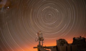 Star trails creating a circular pattern in an orange sky, viewed from a window inside the International Space Station.