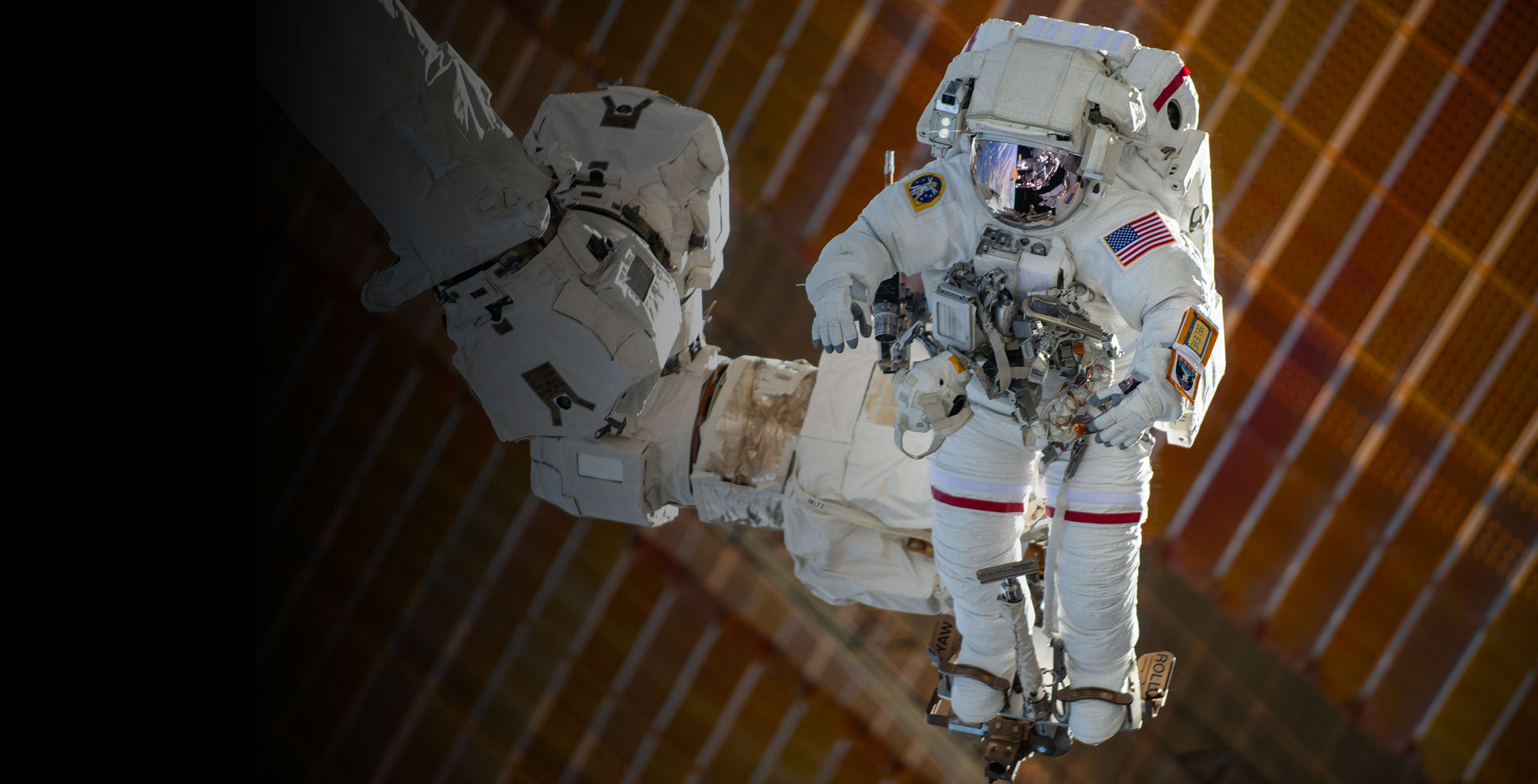 Astronaut in an Extravehicular Mobility Unit spacesuit attached to a large robotic arm outside the International Space Station