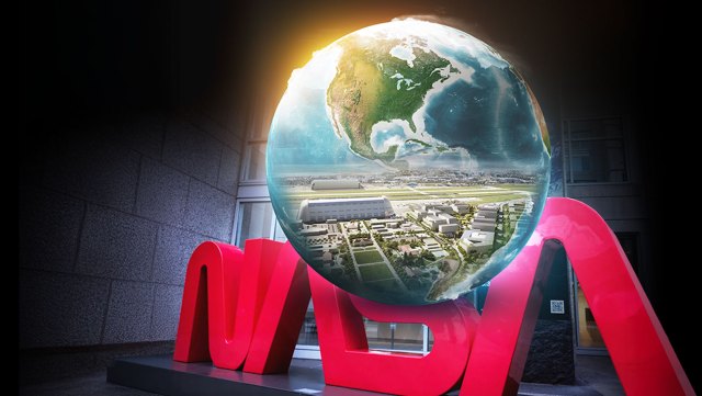 Illustration of a globe containing a bird's-eye view of buildings. The globe is on top of a sculpture of the red NASA "worm" logo.