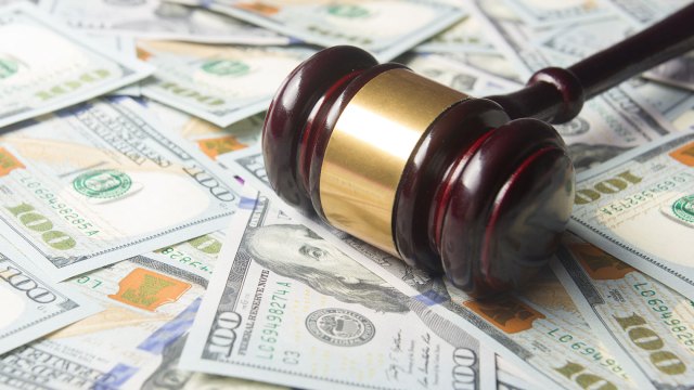 A judge's gavel laying on top of a stack of $100 bills.