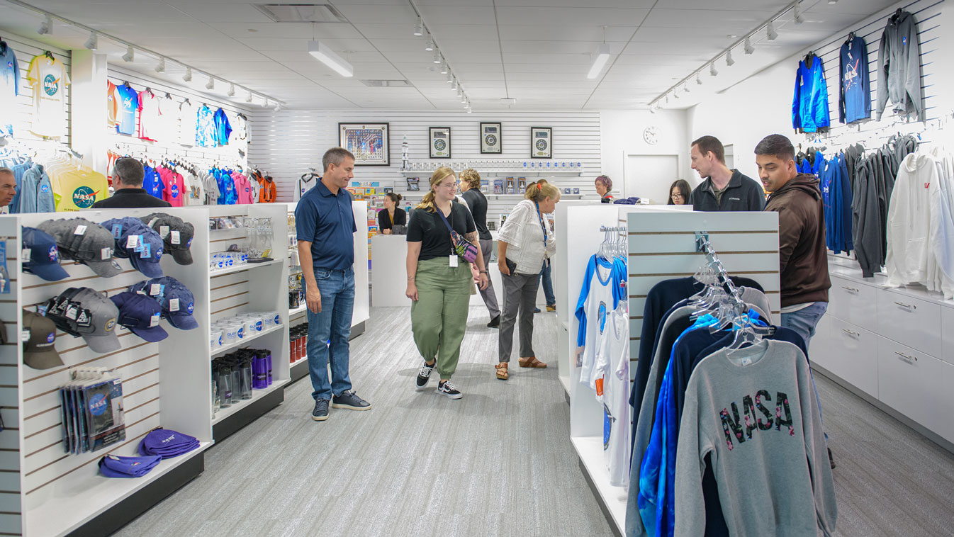 The inside of a NASA gift shop with several customers and NASA hats, shirts, and sweatshirts