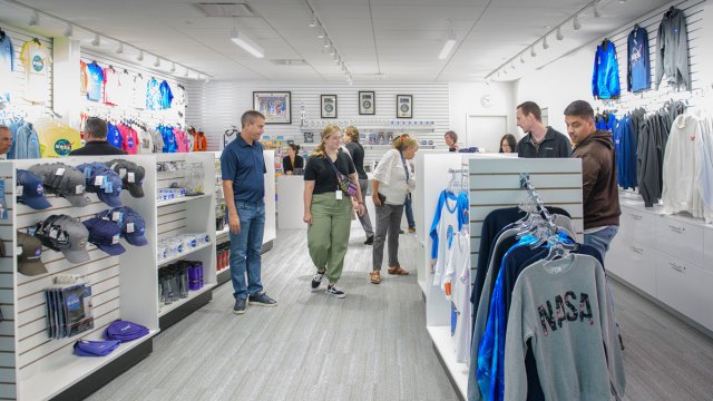 The inside of a NASA gift shop with several customers and NASA hats, shirts, and sweatshirts