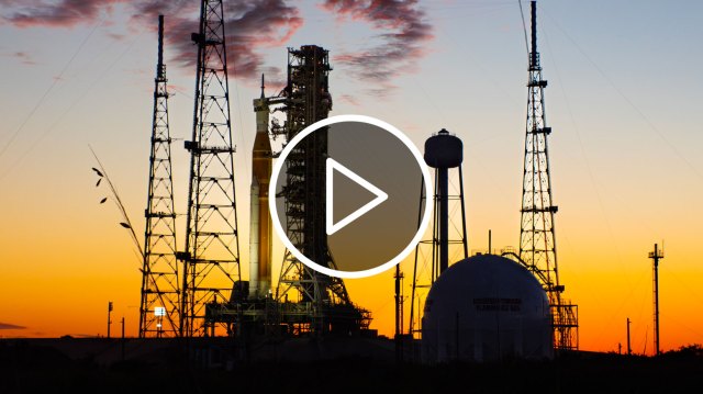 An icon of a play button over an image of NASA’s Space Launch System rocket and Orion spacecraft on a launch pad at sunset